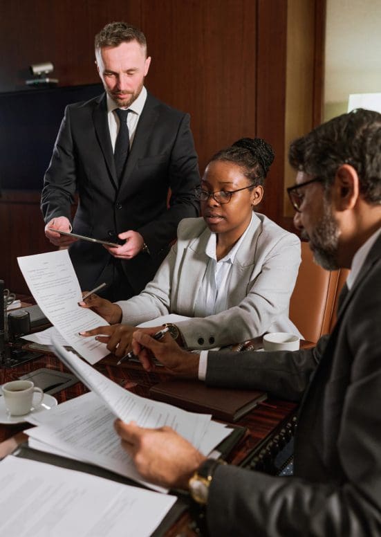 Three professionals reviewing documents in a formal meeting.